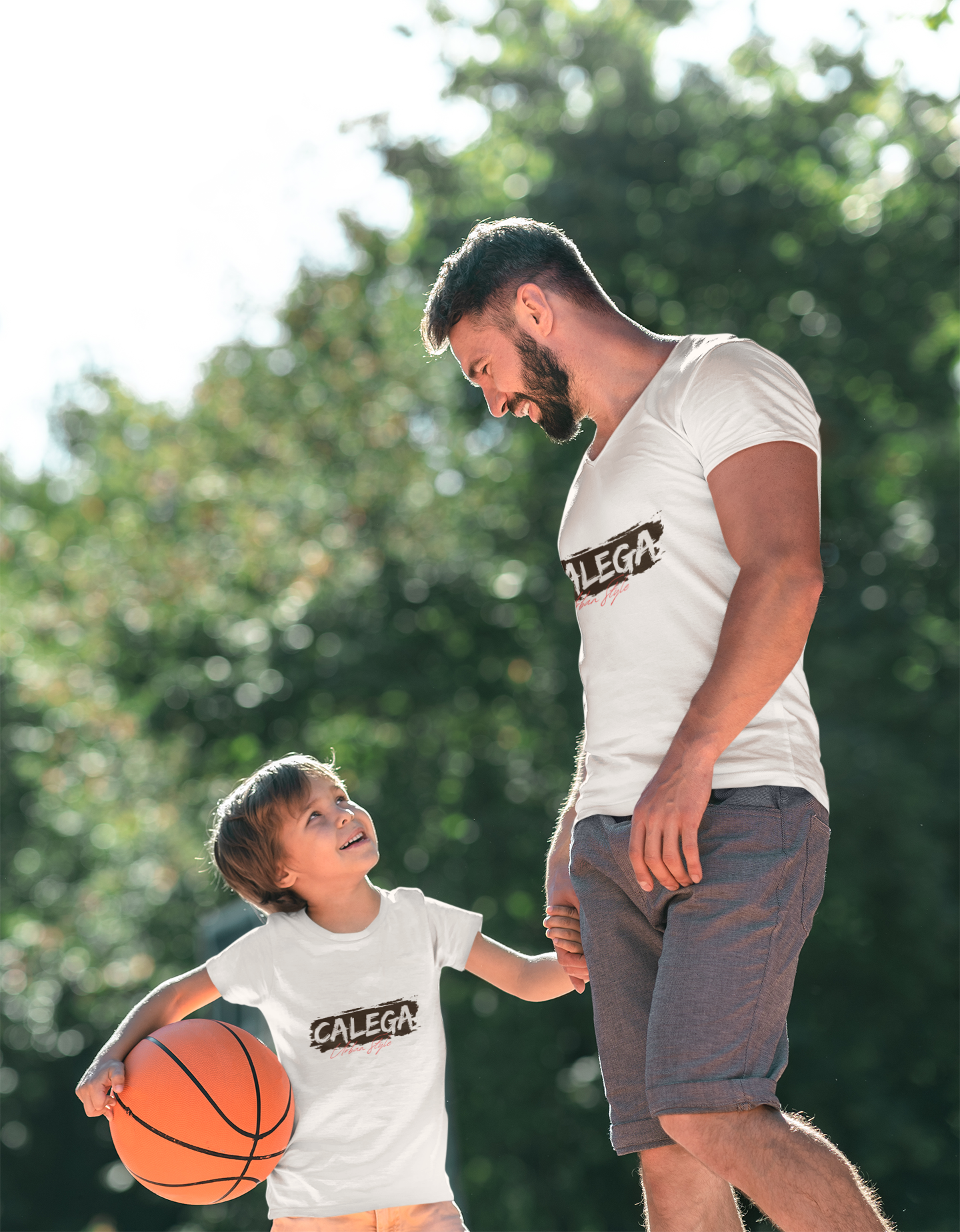 Père et enfant stylés portant un T-shirt unisexe CALEGA dans un décor urbain, incarnant la complicité et l’élégance streetwear intergénérationnelle. Le design représente un père et un enfant de face